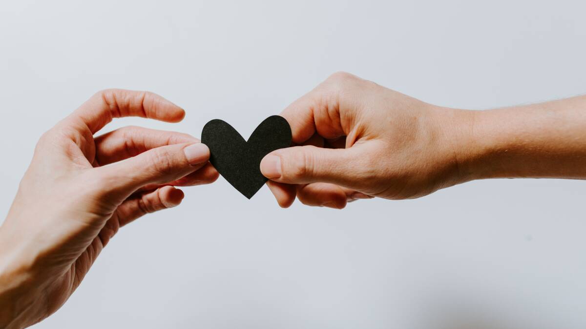 One hand passing a black heart to another hand. Photo by Kelly Sikkema on Unsplash. 